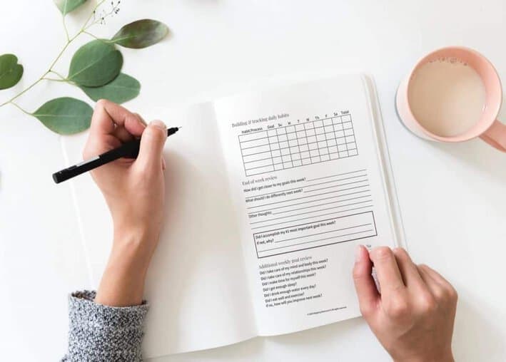 Desktop view of a woman writing in a 30-Day Goal Setting Planner