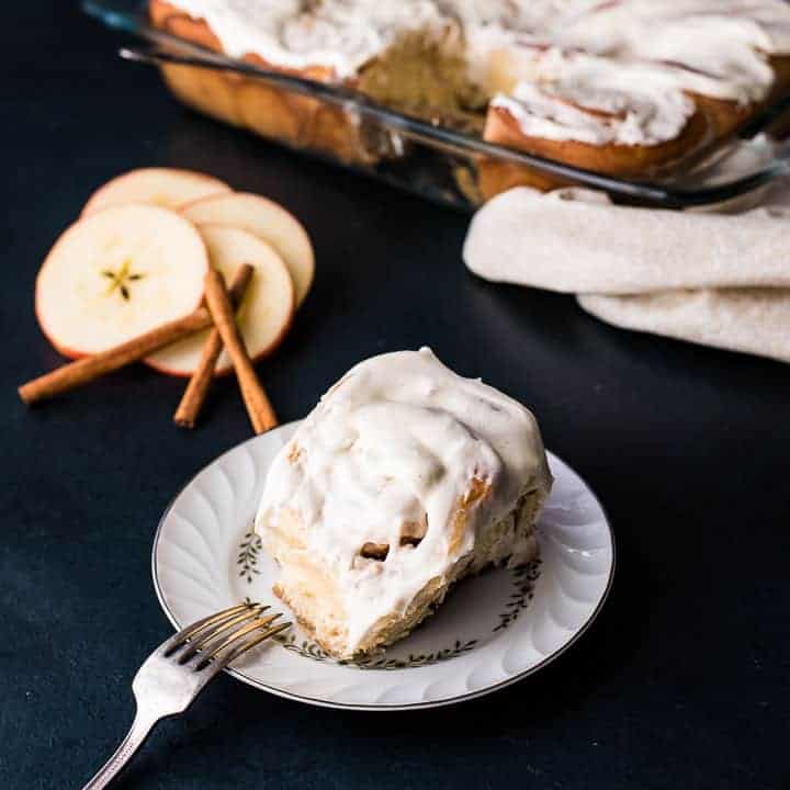 An apple cinnamon roll with vanilla bean cream cheese icing on a white plate with a blue background.