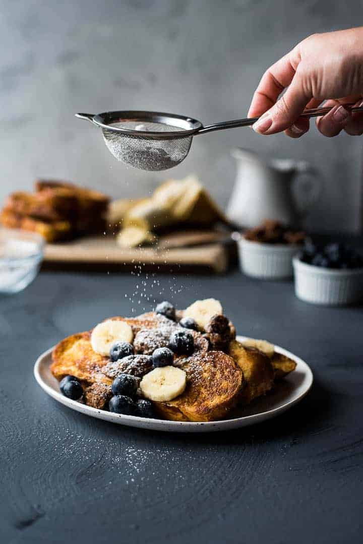 A serving of vanilla french toasted with fresh fruit being dusted with powdered sugar.