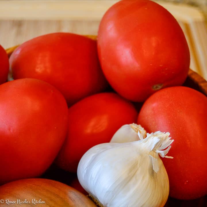 A close up of roma tomatoes and a head of garlic.