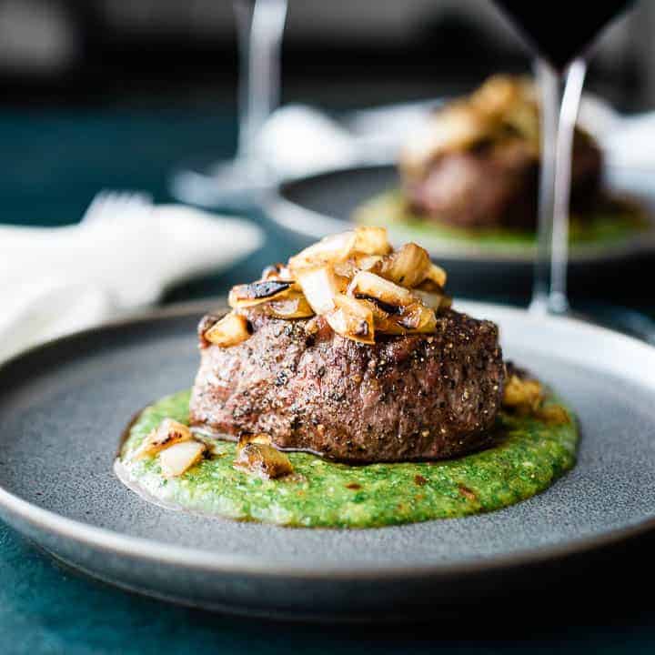 A thick cut filet mignon, resting on a green colored peach mango cilantro sauce and topped with grilled onions.