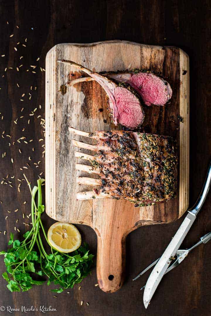 Overhead shot of a full roast rack of lamb on a wooden cutting board with two chops on the side.