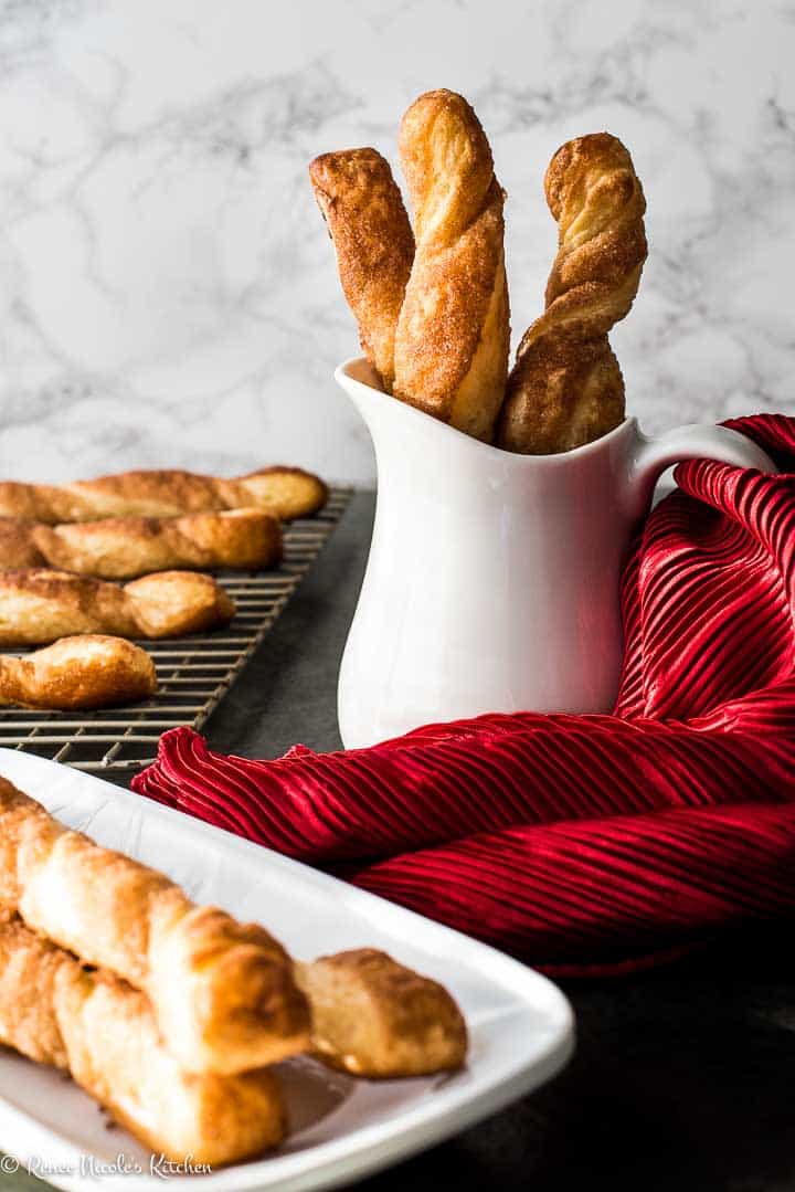 Cinnamon twists in a white jar, on a serving tray, and a cooling rack wth a red satin napkin.