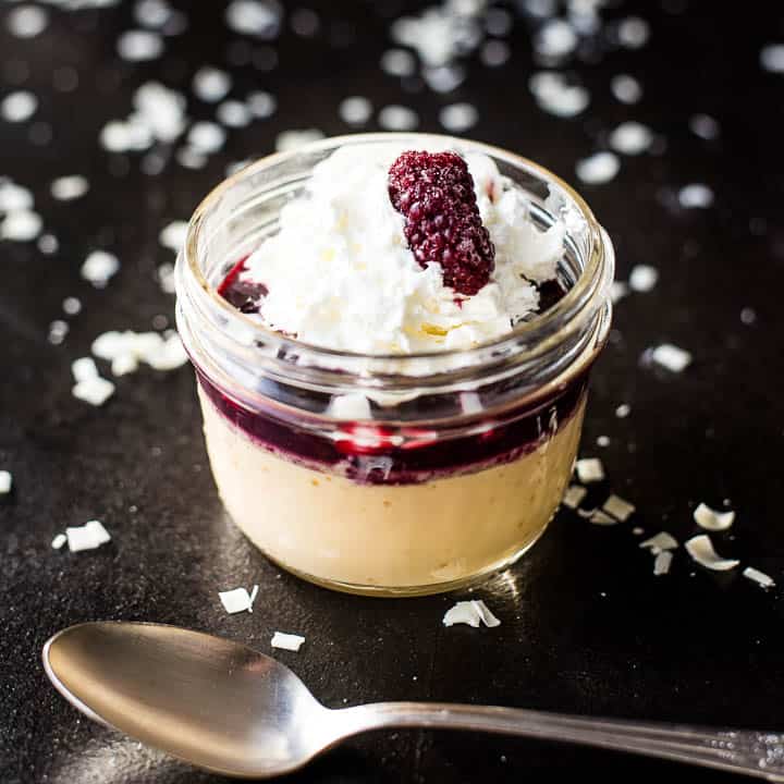 Square image of blackberry white chocolate pots de creme in a glass jar surrounded by white chocolate shavings.