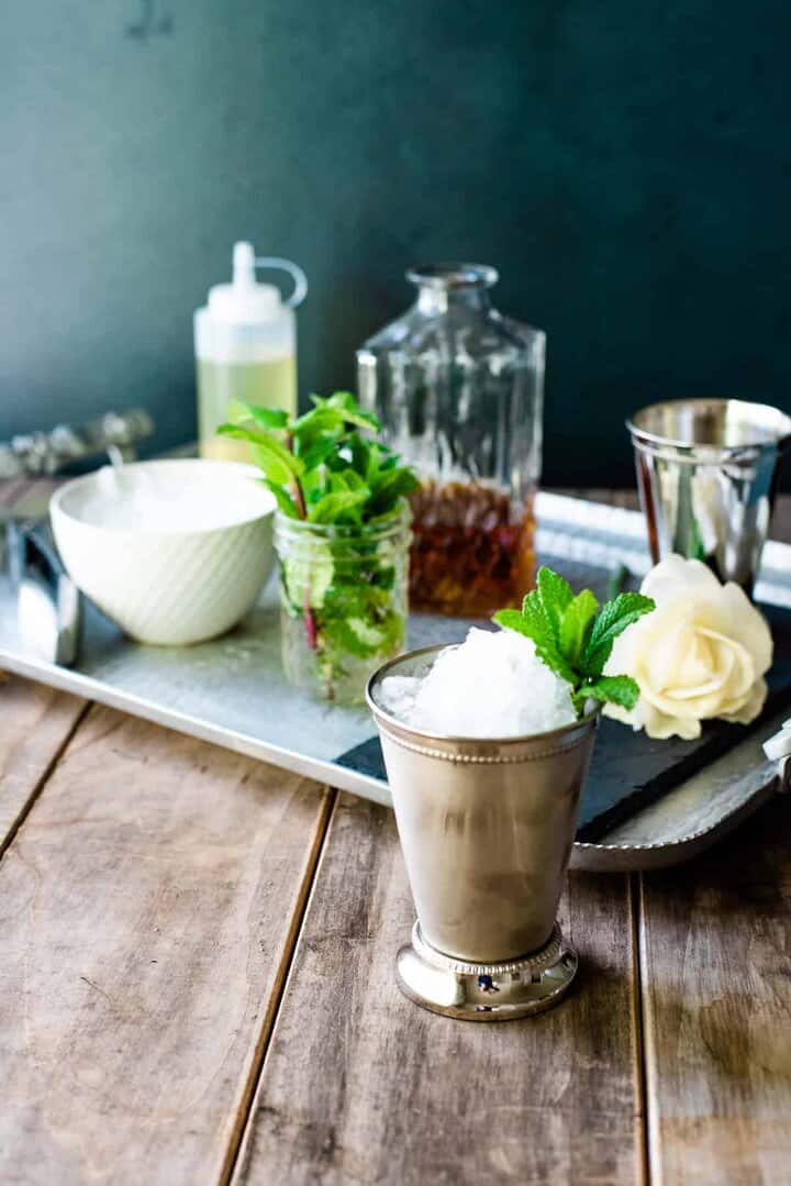 A finished mint julep in front of a silver tray set up with all you need to make a Kentucky Derby mint julep bar.