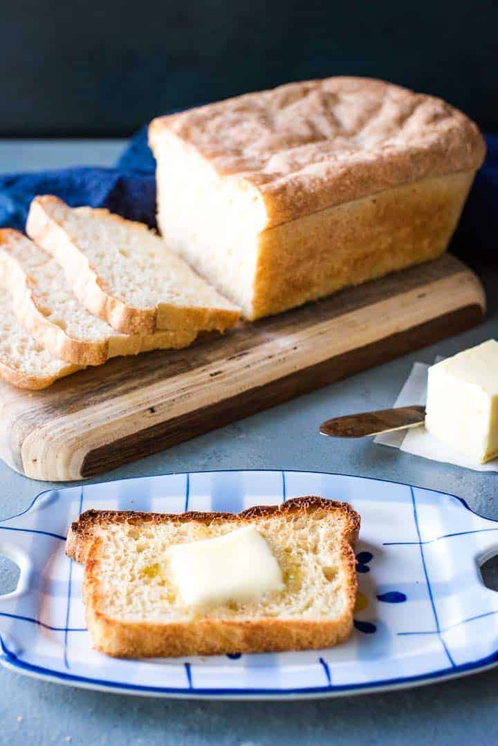 A slice of buttered English muffin bread with the sliced load in the background.