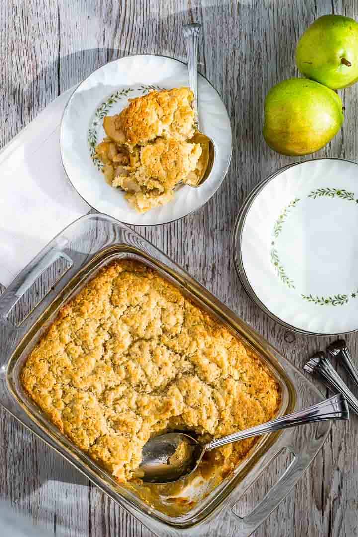 Overhead shot of spiced pear cobbler with one serving dished into a plate and an empty plate waiting to be filled.