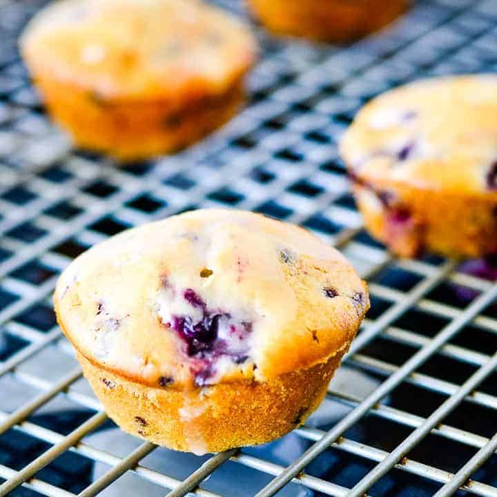 A close up of a blackberry muffins drizzled with lemon glaze sitting on a gray cooling rack on a dark background.