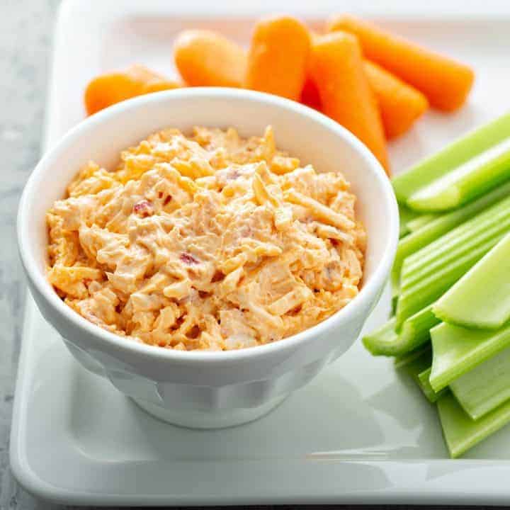 white bowl filled with southern pimento cheese spread on platter with carrots and celery