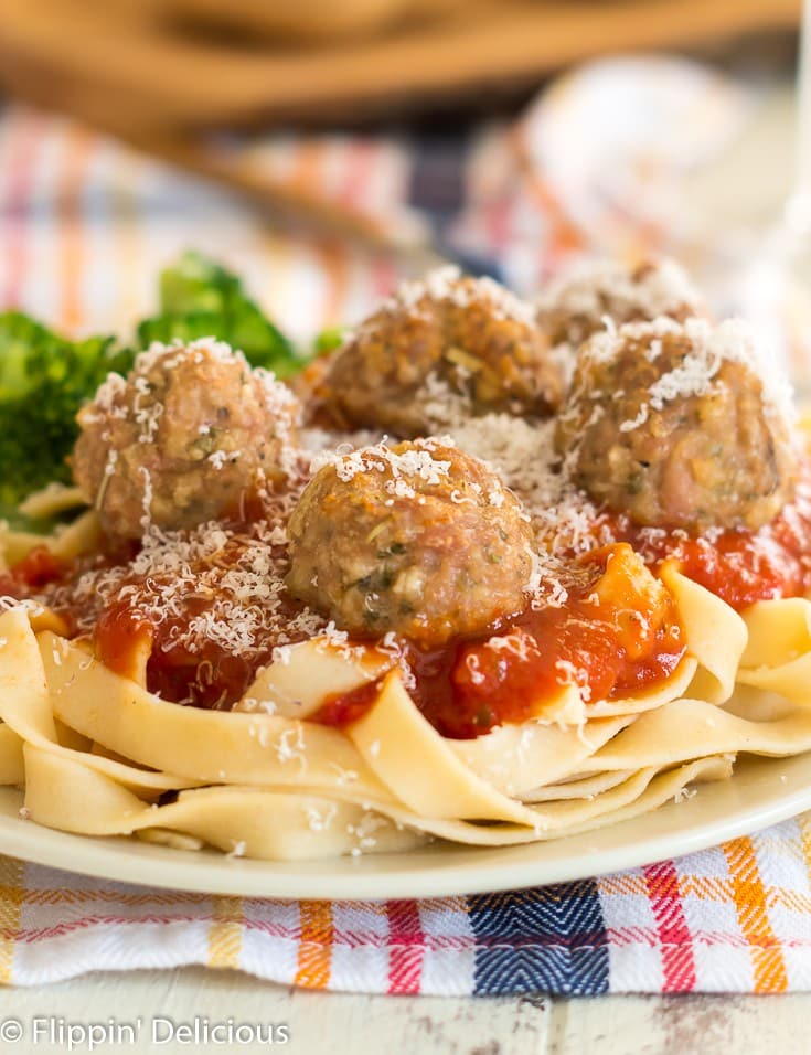 close up of gluten free baked turkey meatballs on a bed of gluten free fettucine covered in marinara sauce