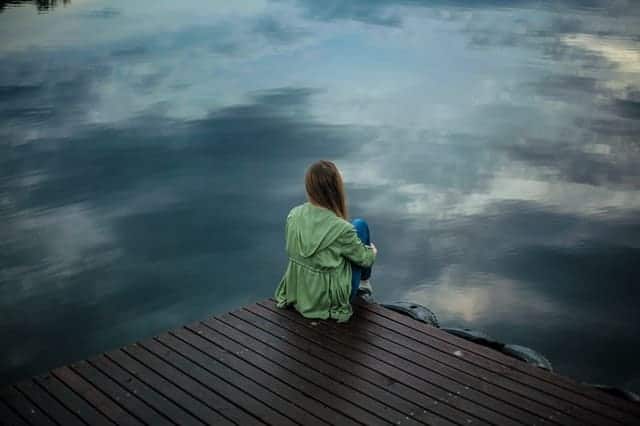 una donna si siede sul bordo di un molo e guarda nell'acqua