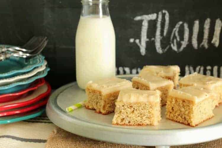 Banana Sheet Cake with Browned Butter Frosting cut in squares on serving tray with milk