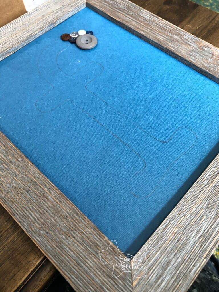 blue scrap book paper placed in wood frame with buttons glued onto the start of the letter f
