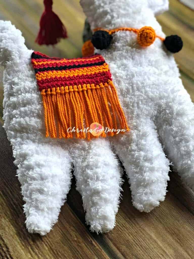 picture of fuzzy white crochet llama with orange red striped blanket