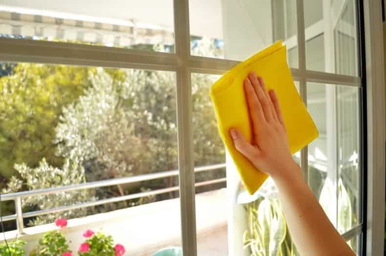 an arm and hand holding a yellow cloth, spring cleaning a window from inside an apartment
