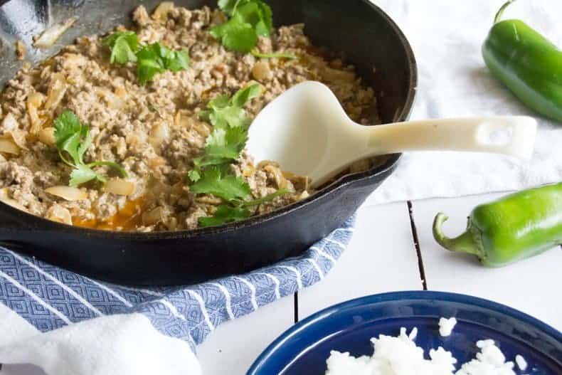 Creamy green chili ground beef in a skillet with rice on the side, and chili peppers beside them