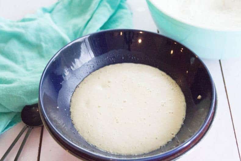 Pizza dough ingredients proofing in a dark blue bowl. An aqua tea towel is nearby.