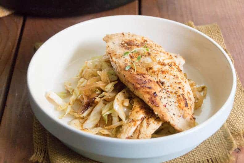 A white bowl with a bed of chicken and cabbage noodles.