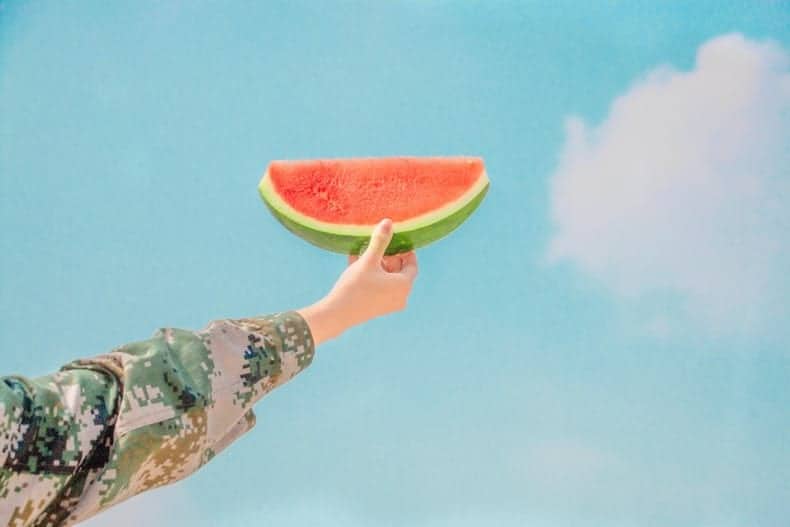 arm holding up a hunk of watermelon against a blue sky
