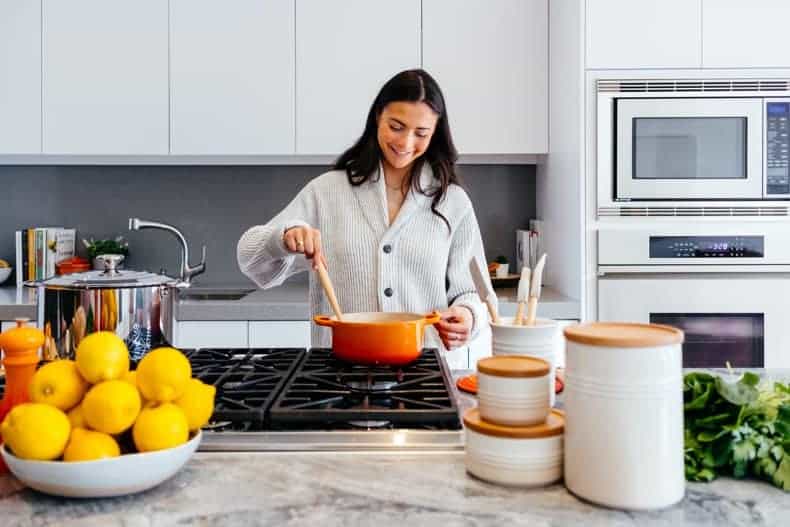 woman cooking a quick and easy meal with an orange pot, with a white kitchen