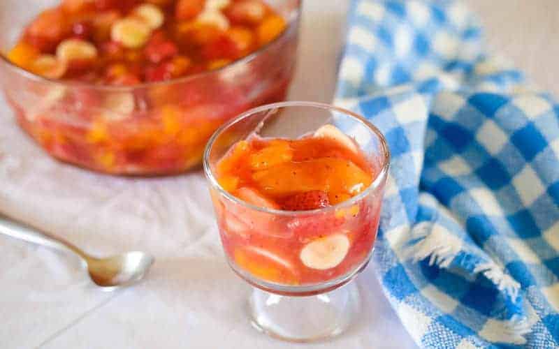 fruit salad with peach pie as a filling in a glass bowl with a blue and white napkin on table