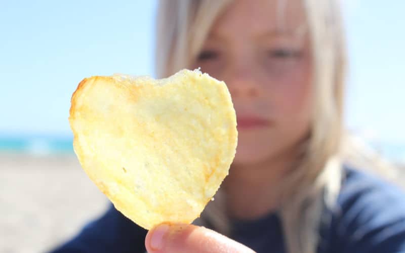 girl holding up chip at the beach as a beach food snack idea