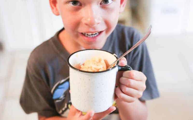 child holding white mug filled with orange pineapple churned ice cream