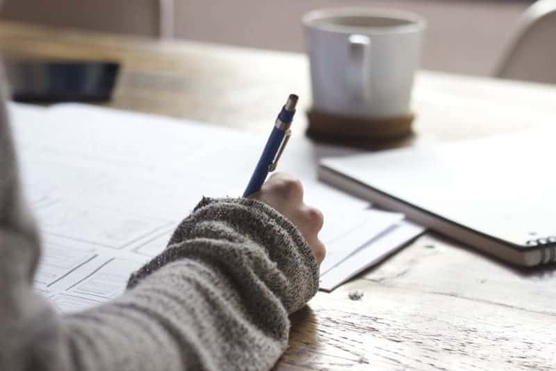 Woman's hand writing with a pen and paper at a table.