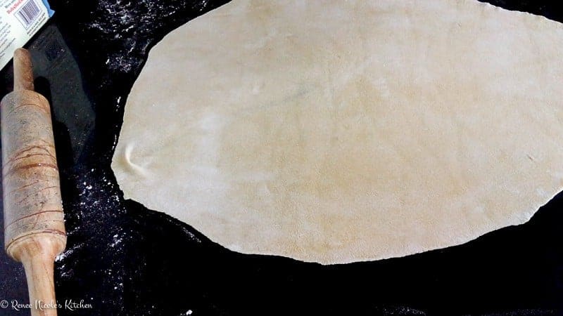 A large sheet of pasta dough rolled into an oval on a black background.