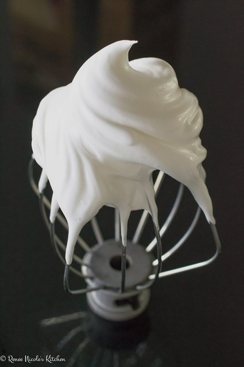 The wire whisk attachment from a kitchenaid mixer covered in swiss meringue.