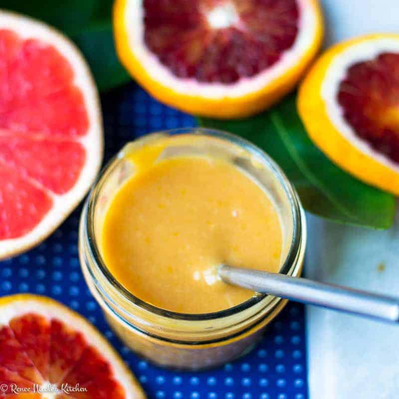 Grapefruit and blood orange curd in a small glass jar next to slices of fresh grapefruit and blood oranges.