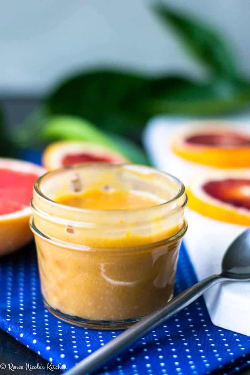 A jar of grapefruit and blood orange curd in front of slices of grapefruit and blood orange.