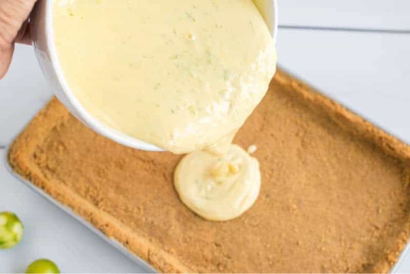 pouring key lime pie batter into a graham cracker crust on a jelly roll pan