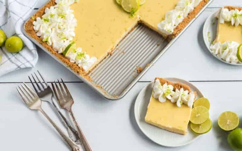 key lime slab pie with shipped cream and graham cracker crust on white table