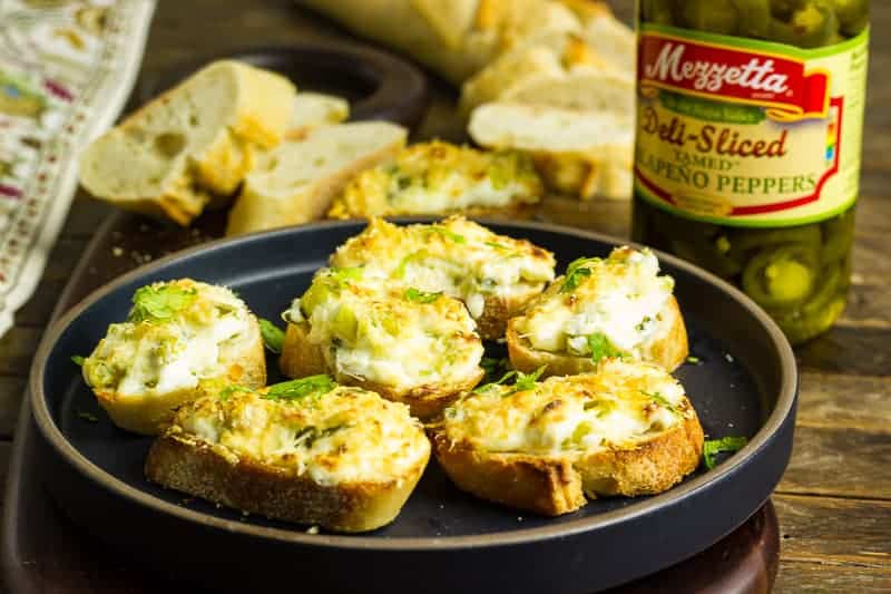 Jalapeño Relish Cheesy Toasts Jalapeno Relish Cheesy Toasts on a black plate that sits on a wooden table.