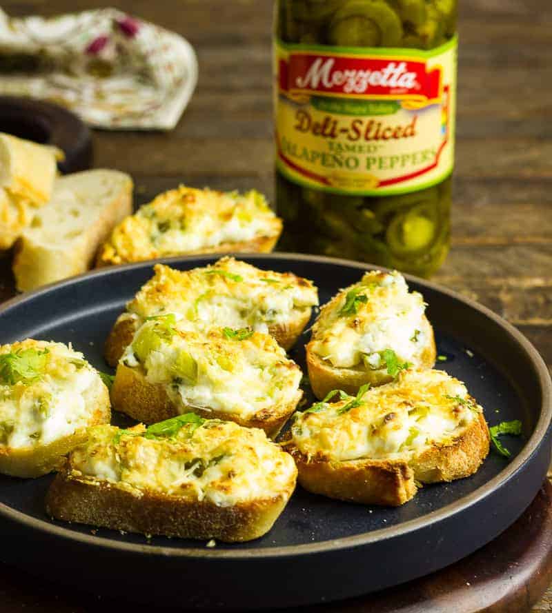 Jalapeño Relish Cheesy Toasts Jalapeno Relish Cheesy Toasts on a black plate that sits on a wooden table.