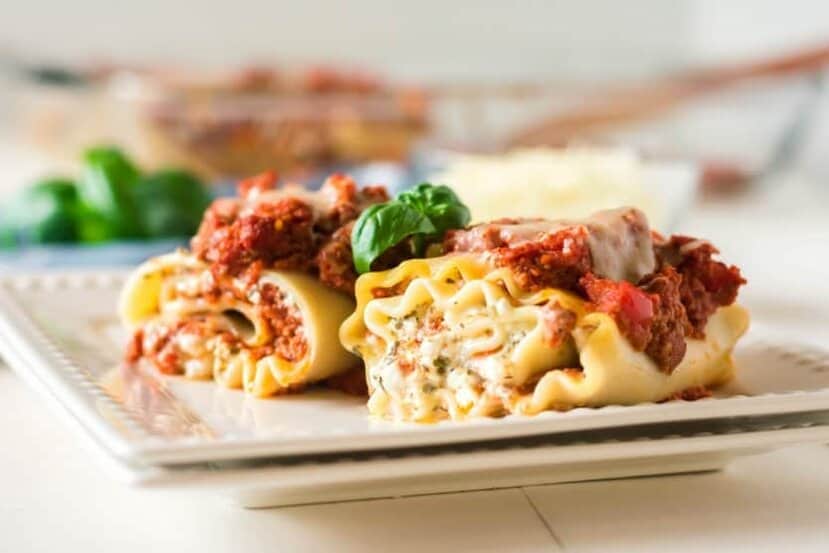close up of beef and pepperoni lasagna rolls with cottage cheese on a white plate