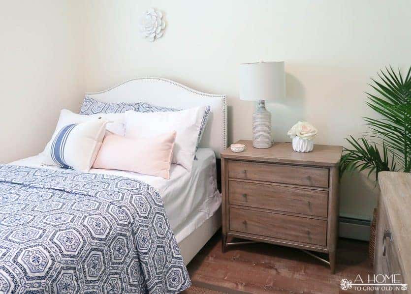 white upholstered bed with blue and white patterned quilt and wood nightstand with lamp