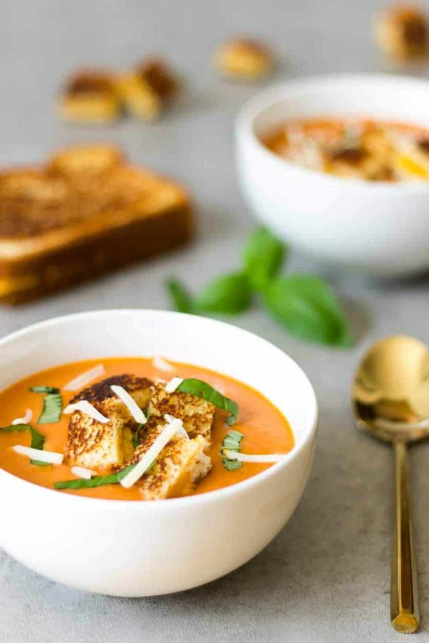 several bowls of creamy tomato homemade soup with grilled cheese in the background
