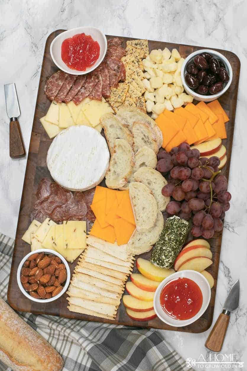cheeseboard with salami, cheddar, brie, pepper jack, olives, pepper jam, goat cheese, grapes and apples
