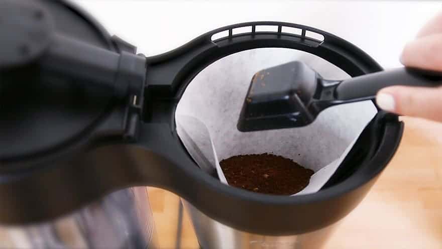 Scooping ground coffee into the filter of a drip brewer