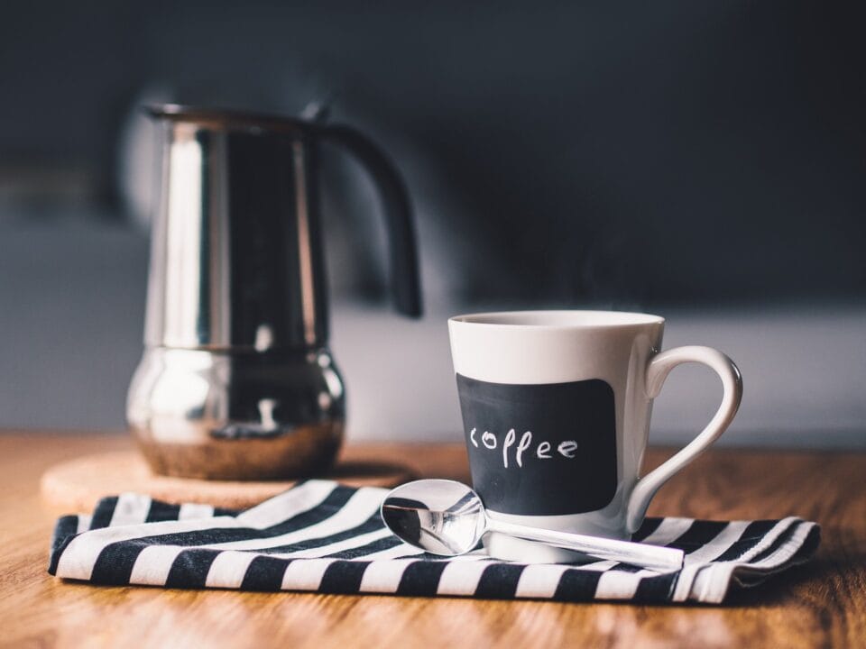 a coffee cup with coffee written on it and a jug behind it
