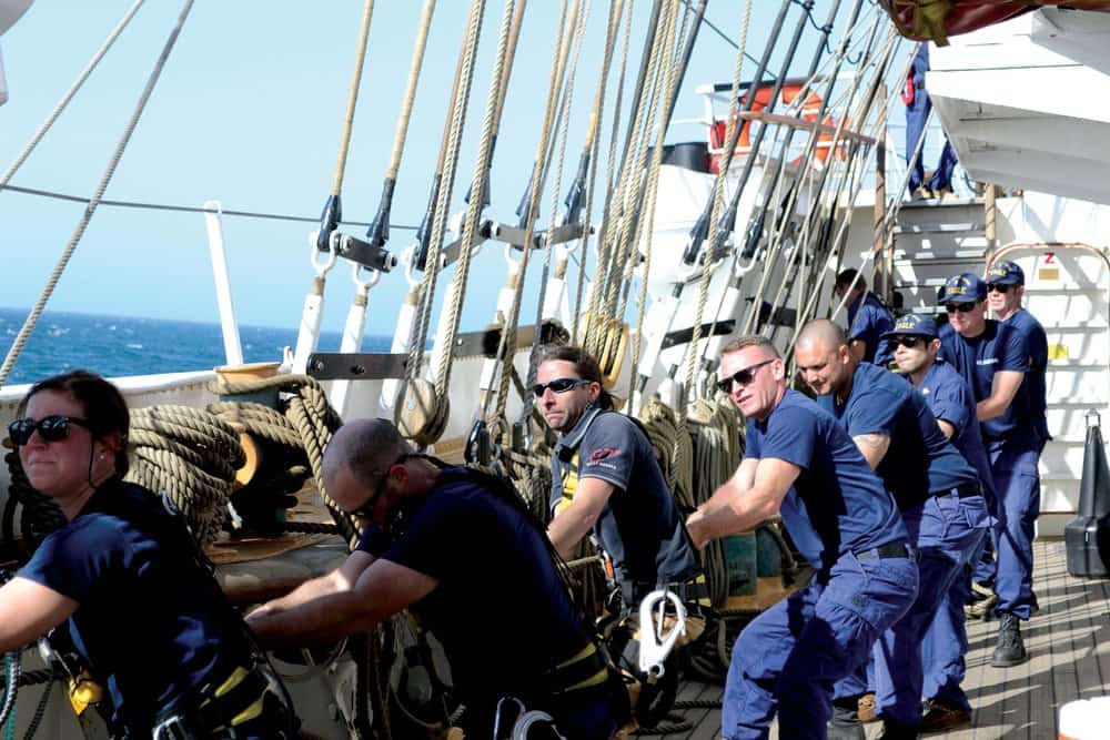 Justin Ailswoth (third from left) and Coast Guard crewmembers haul up one of the Eagle ’s 23 sails.Photo by Karen Soule.