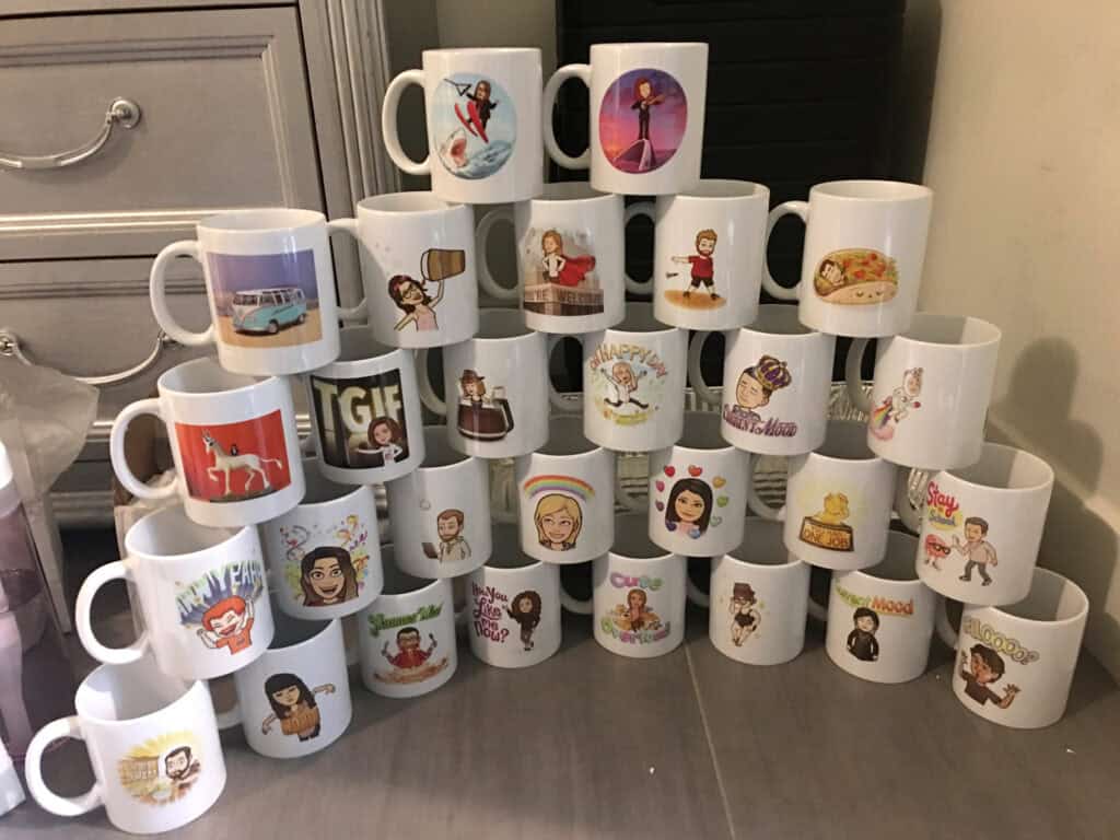 Shot of white mugs stacked in a pyramid, each personalized with a bitmoji for that person.