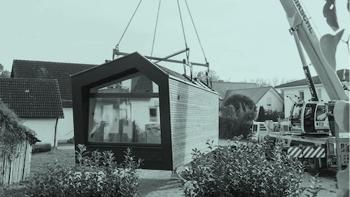 tiny-house-marktstudie-livee-transport-tiny-house Das Bild zeigt ein Tiny House, dass auf ein Grundstück mit einem Schwerlastkran gehoben wird