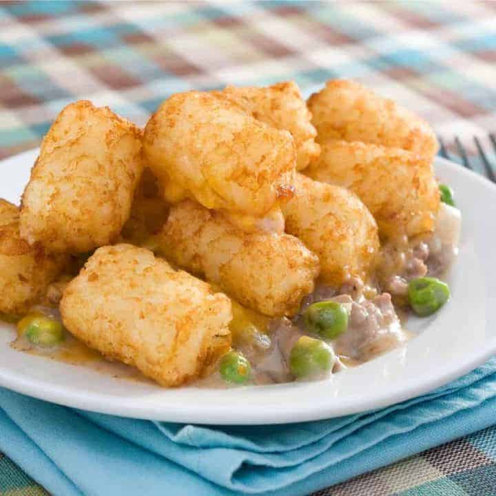 tater tots, ground beef, cream of mushroom soup and peas on white plate with blue napkin