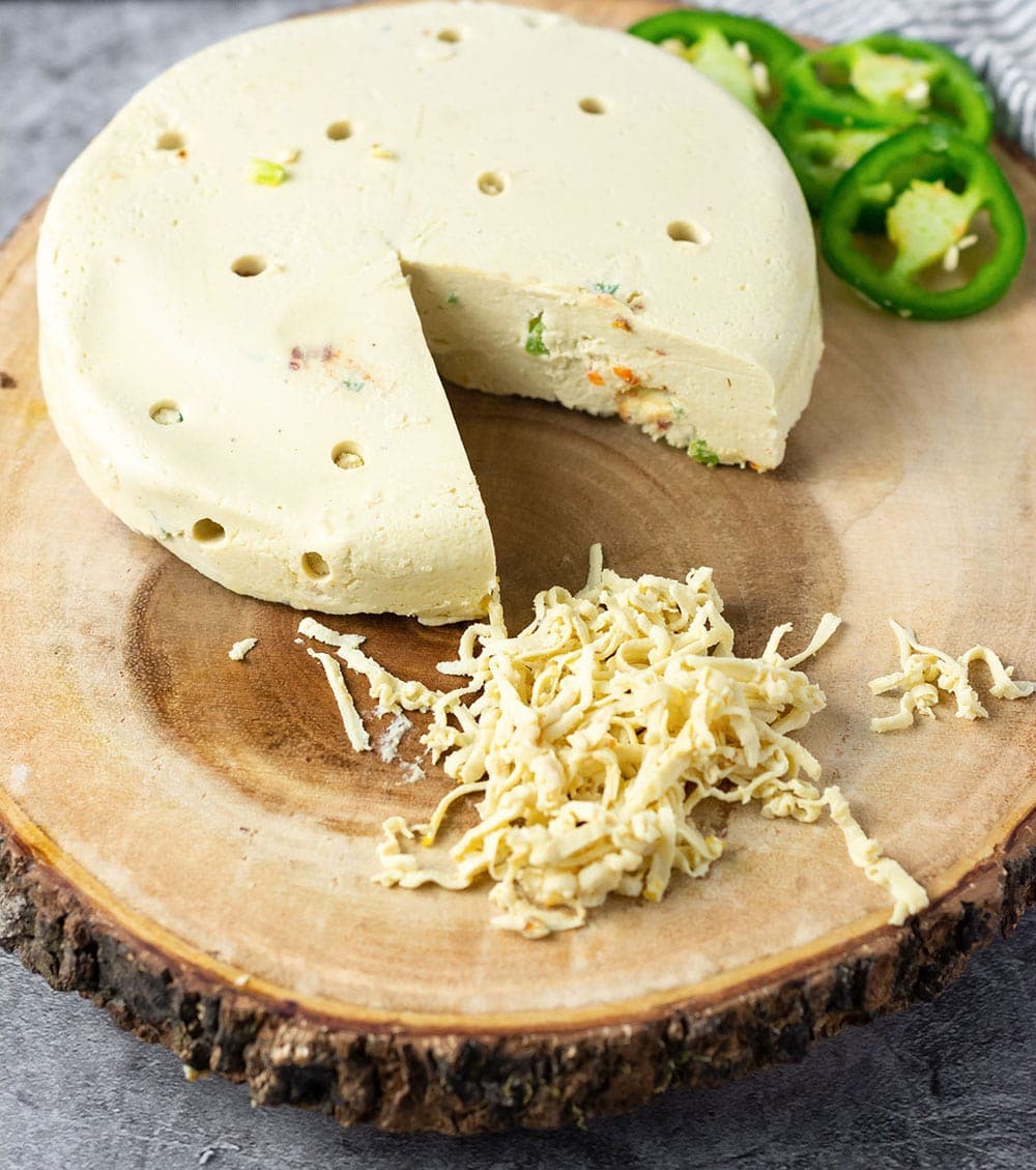 homemade vegan pepper jack cheese that can grate on a cutting board with jalapeno slices as garnish