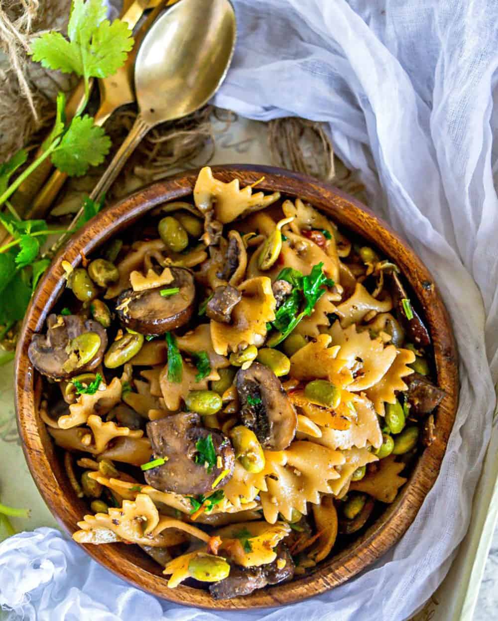 Edamama Mushroom Pasta salad in a brown bowl garnished with cilantro on a white background