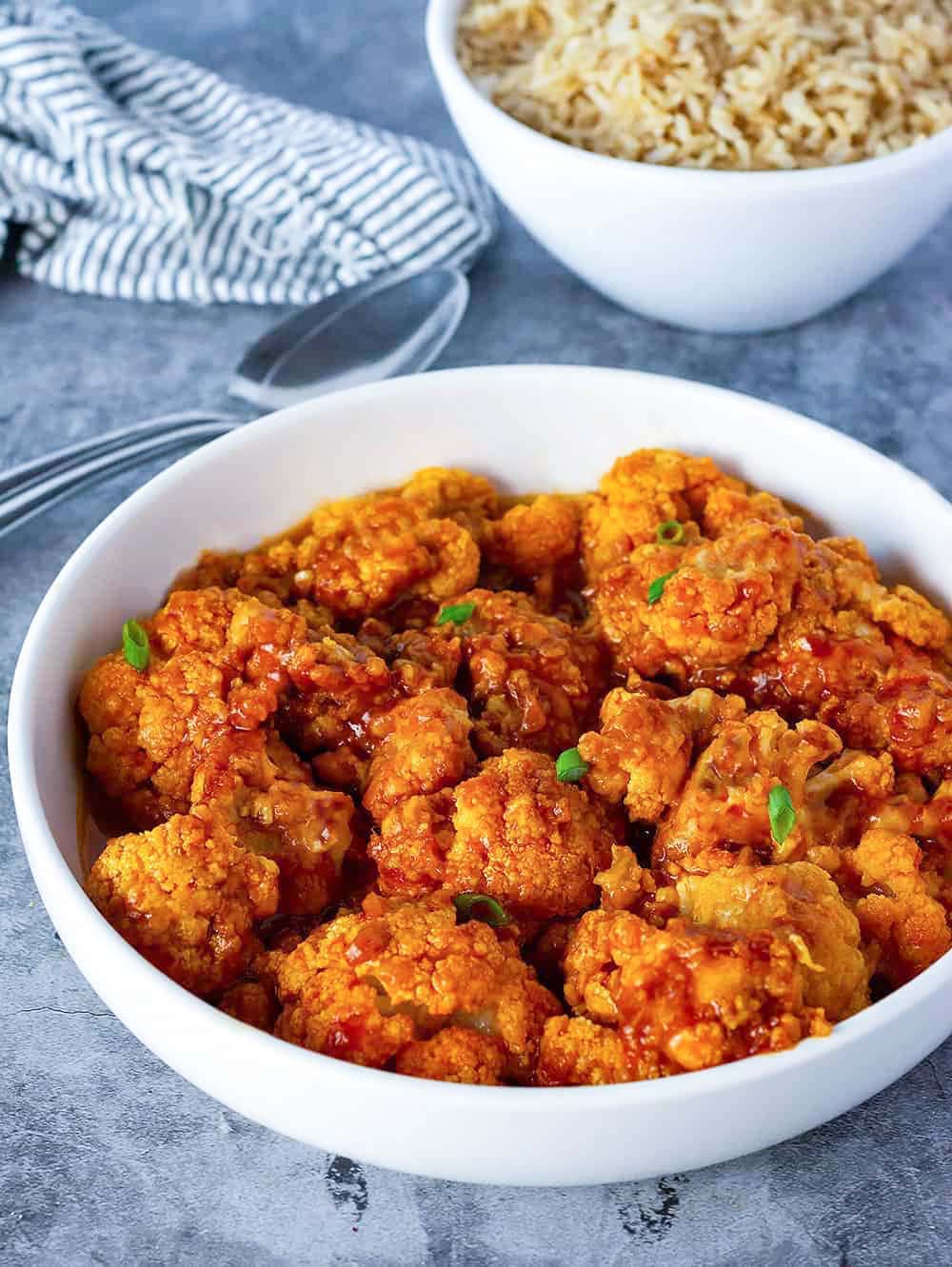 General Tso's Cauliflower in a white bowl with a white bowl of rice in the background