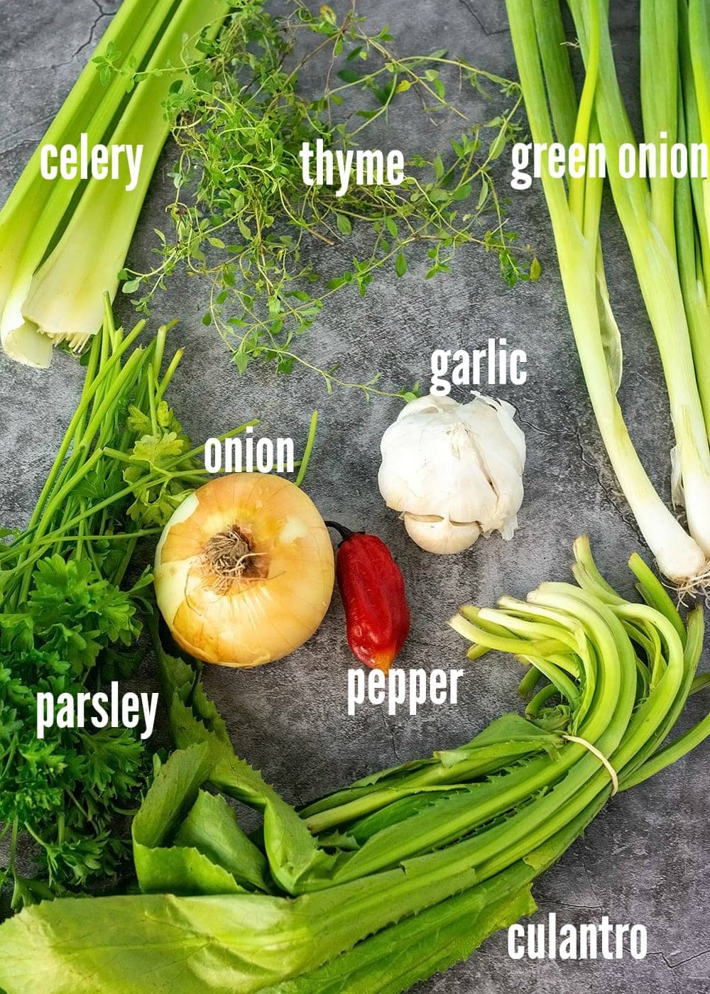ingredients for green seasoning on a grey marbled background, celery, thyme, scallion, onion, pepper, garlic, culantro. parsley
